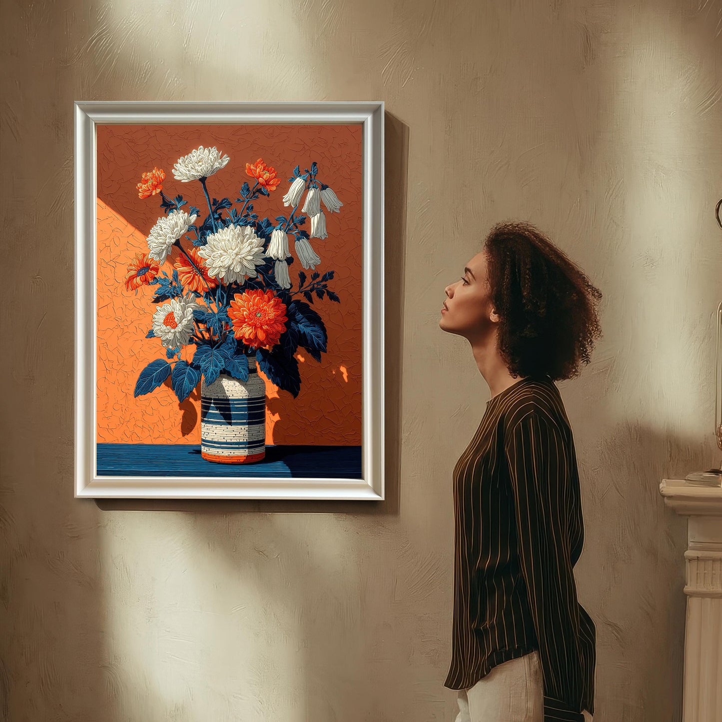 A woman with curly hair stands in a room, looking at a framed floral art print with a white frame that is hanging on a wall.