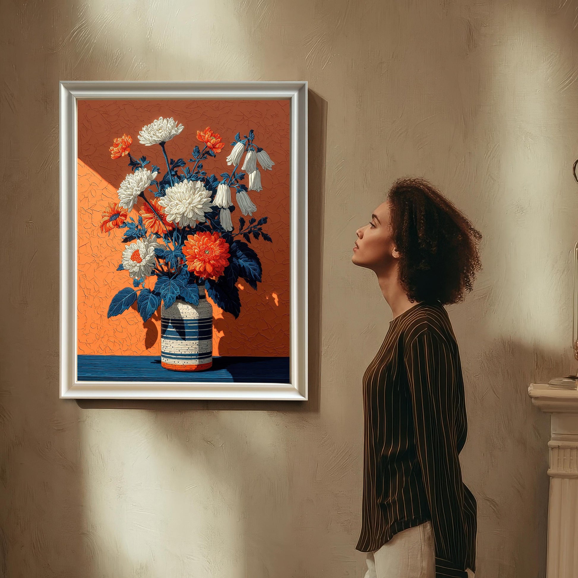 A woman with curly hair stands in a room, looking at a framed floral art print with a white frame that is hanging on a wall.