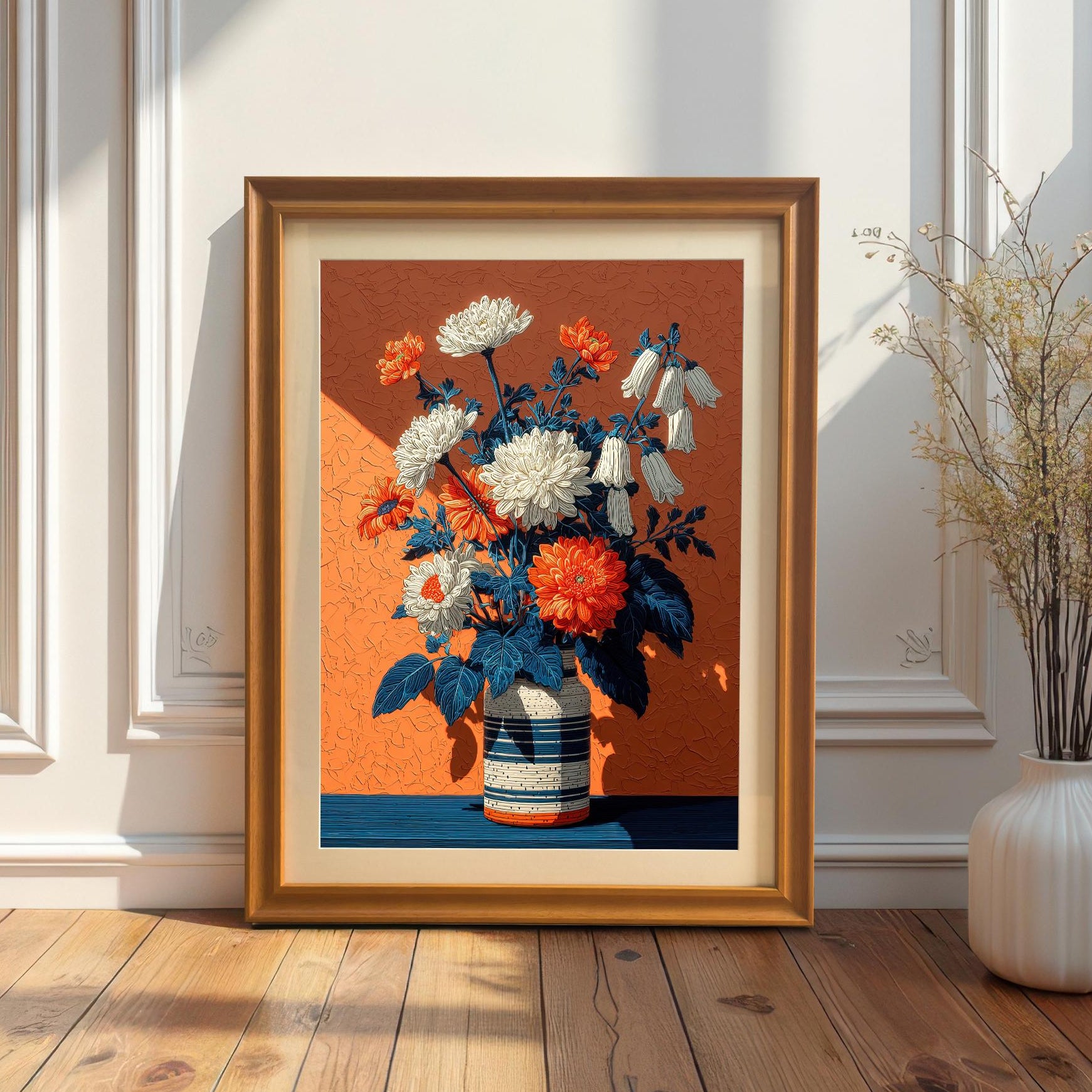 A framed art print of white and orange flowers in a striped vase on a vibrant orange background, with a natural wood frame, leaning against a white wainscoting wall.