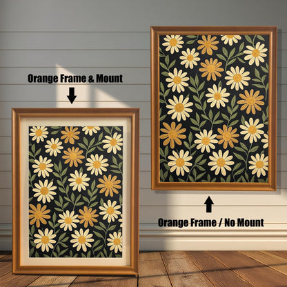 Two orange-colored framed art prints with a pattern of yellow flowers on a dark background. One has a white mat board and the other does not.
