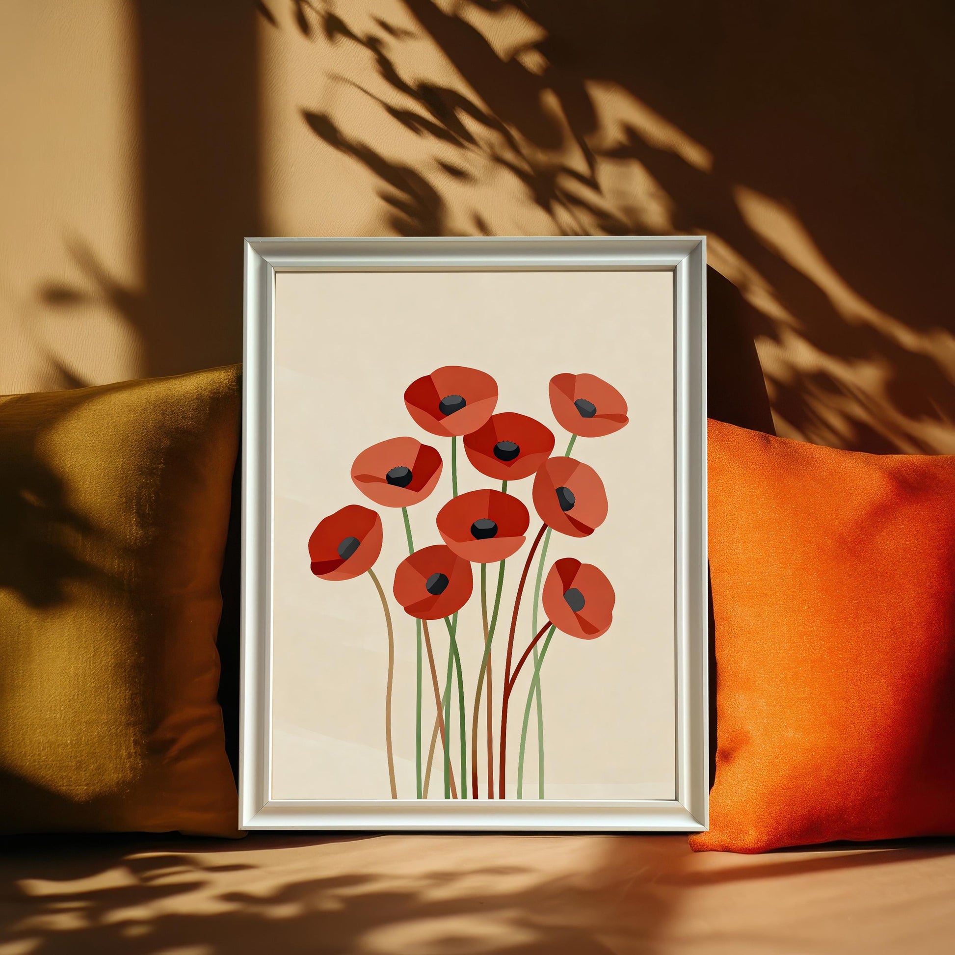 An abstract poppy print in a silver frame leans on a couch, propped between two throw pillows, one gold and one orange.