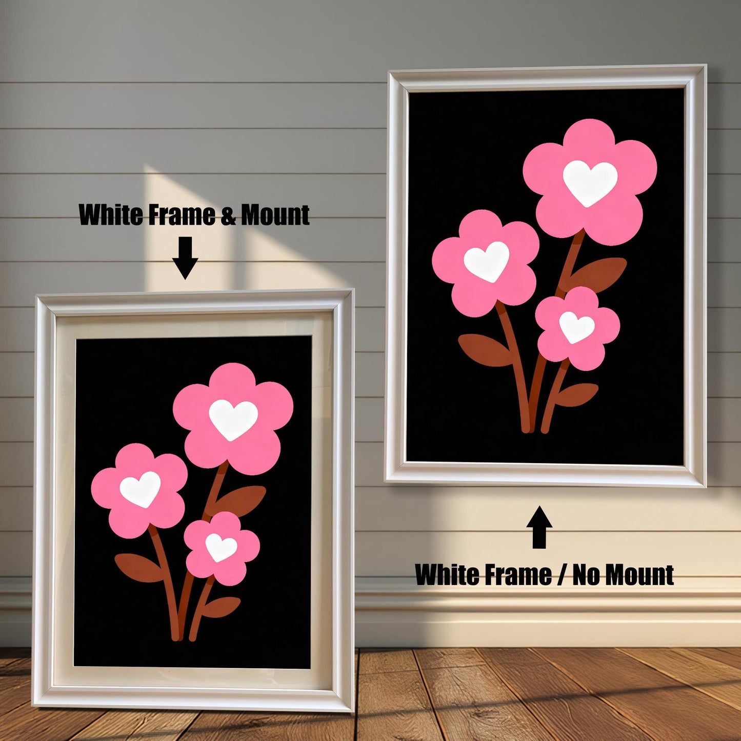 A framed art print of three pink flowers with white hearts is shown in two styles against a wooden wall. One has a white frame with a white mount, the other is a larger size with the same frame, but no mount.