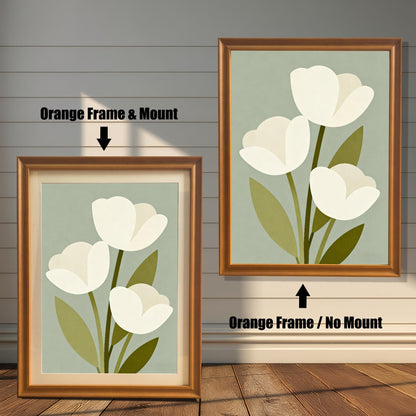 A framed art print of three white tulips is shown in two styles against a wooden wall. One has an orange-colored frame with a white mount, the other is a larger size with the same frame, but no mount.