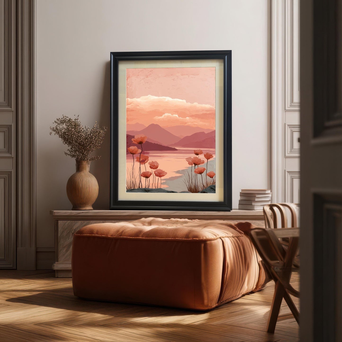 A framed art print of the poppy landscape with a black frame, resting on a console table above a large, soft brown ottoman. The setting is an elegantly paneled room with wood floors.