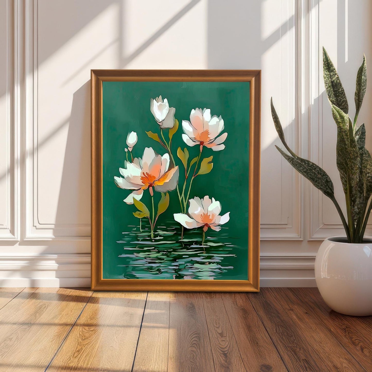 Framed watercolor-style water lily print in an Orange/Gold frame leaning against a white wainscoting wall next to a tall potted snake plant on a wooden floor, with sunlight casting sharp shadows.
