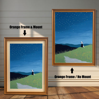 Stylized painting of a black and white dog sitting on a grassy hill under a starry night sky. The image shows two framed options: one on the left with an Orange Frame & Mount (matting), and one on the right with an Orange Frame / No Mount. Both are displayed against a white wood-paneled wall and a wooden floor.