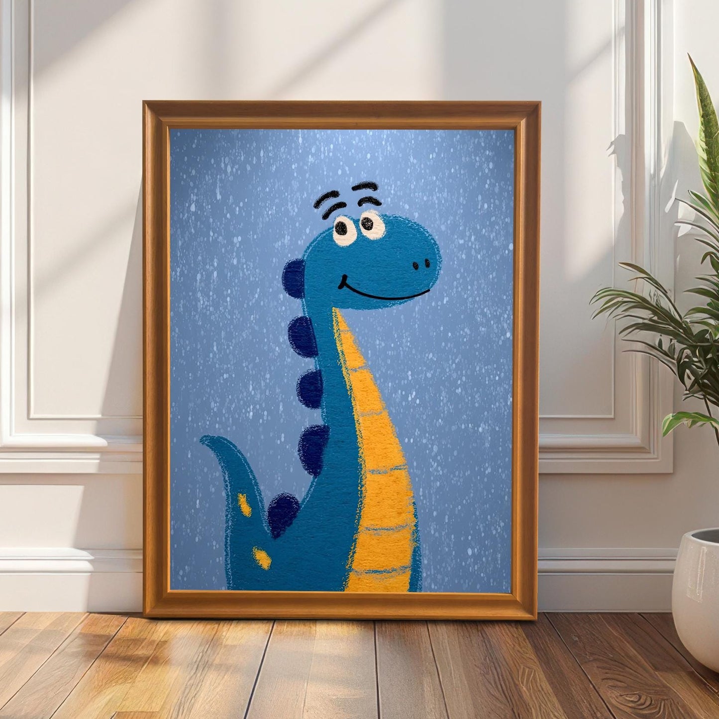 A full-length lifestyle shot of the framed children's art print of a blue and orange cartoon dinosaur standing on a wooden floor, leaning against a white wainscoted wall. The print is in a light brown/orange wood frame. To the right, a tall snake plant (Sansevieria) in a white pot is visible.