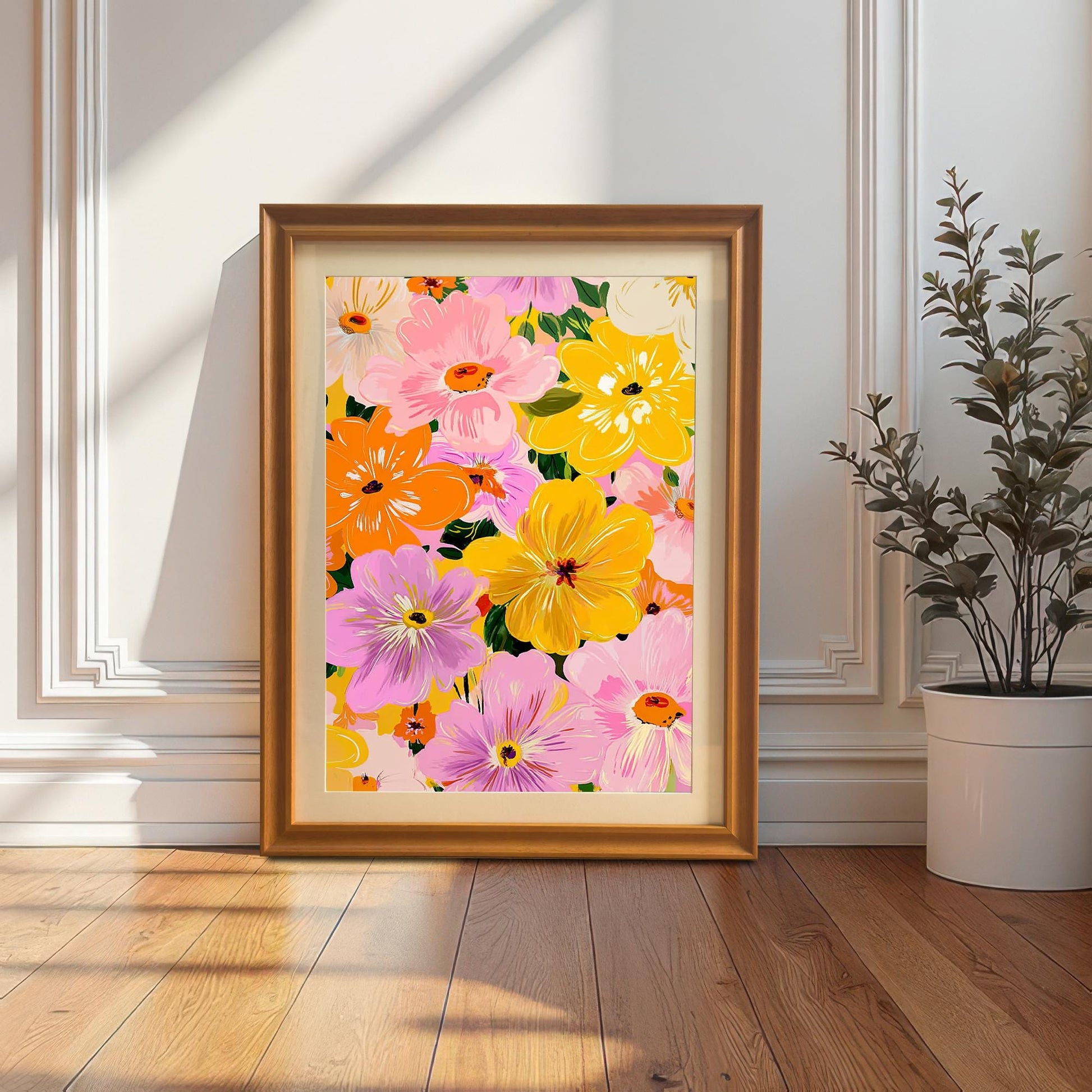 A full-length lifestyle shot of the framed floral art print standing on a wooden floor, leaning against a white wainscoted wall. The print is framed in an orange/gold wood frame. A potted plant is visible on the right.