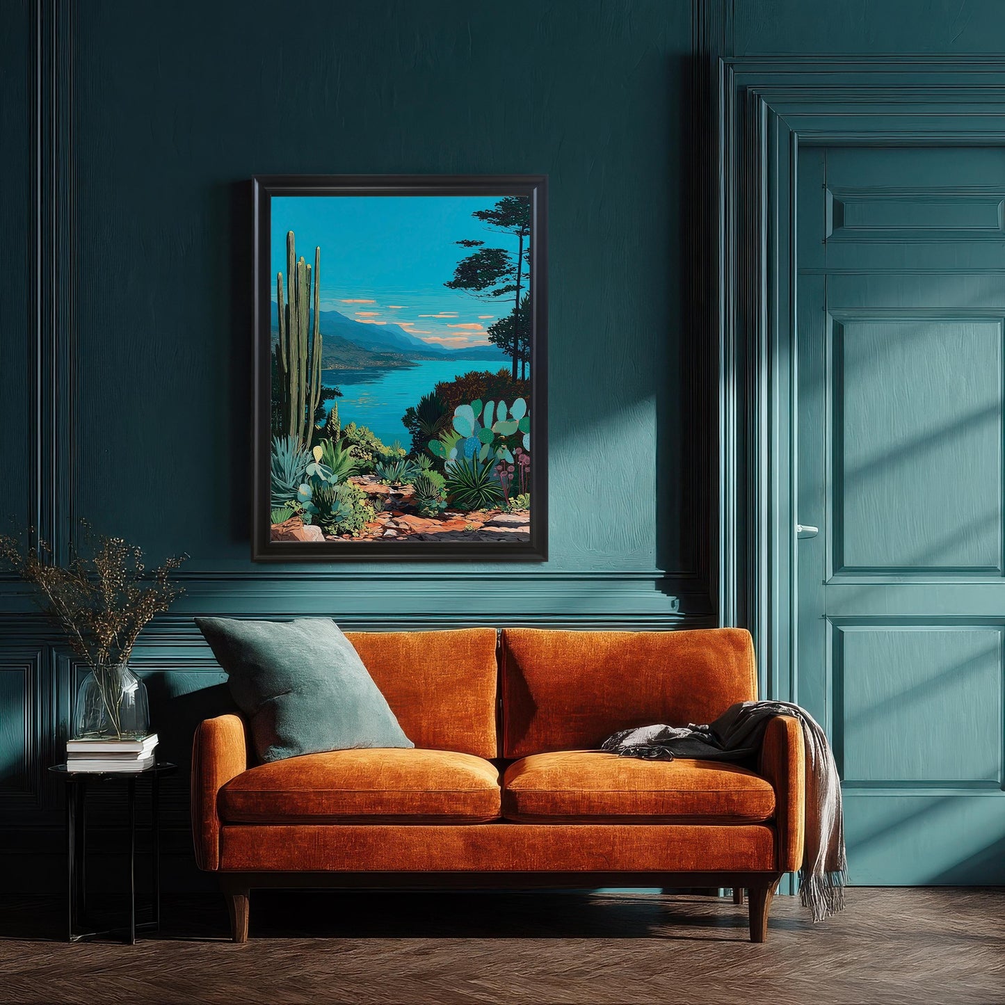 Framed artwork of a vibrant, blue lakeside desert landscape with cacti and succulents, hanging on a dark teal wall above an orange sofa. The frame is black and the room has wainscoting and a matching door.