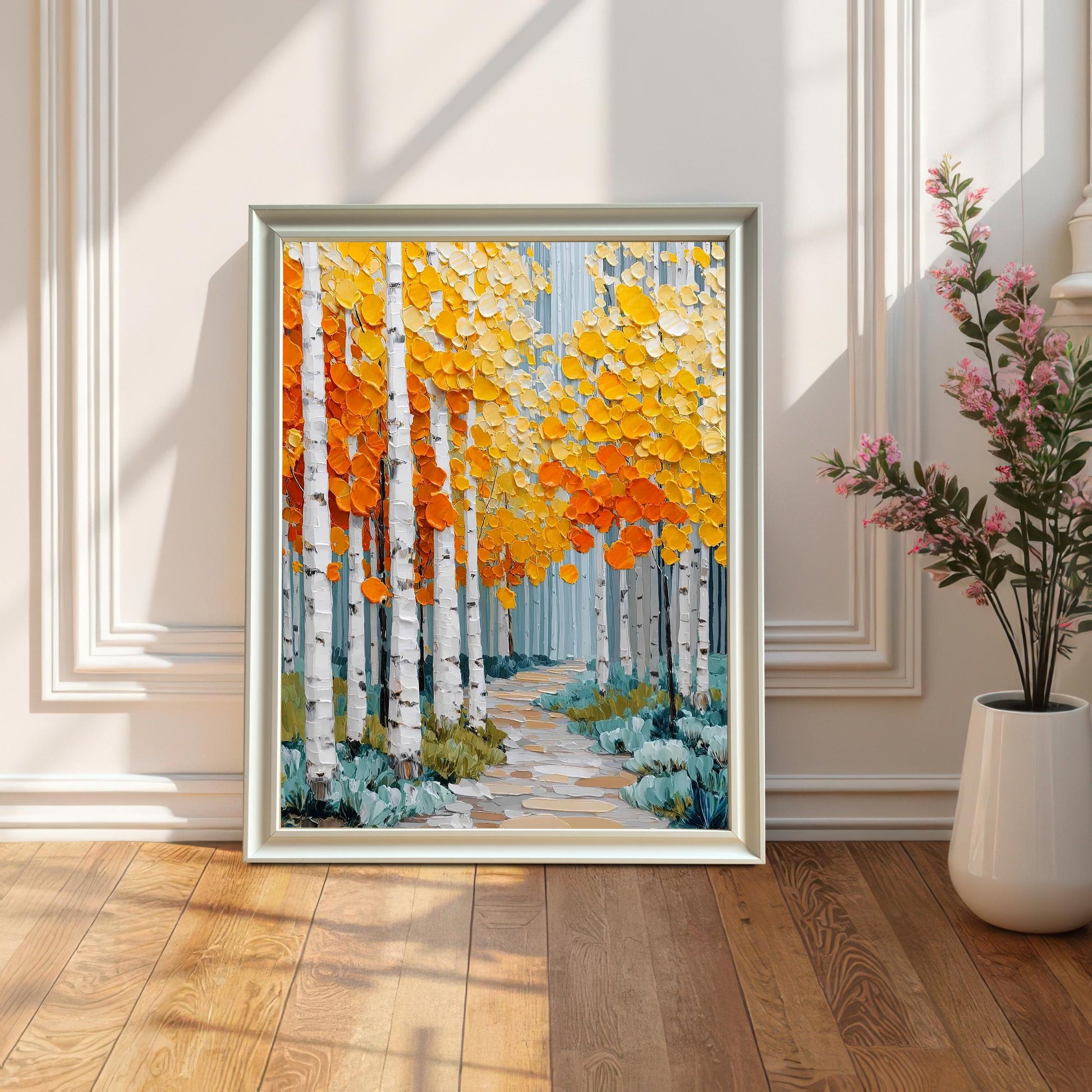 A framed print of an aspen forest leaning on a wooden floor against a white paneled wall. The frame is white. Sun shadows fall across the art and the floor. A white vase with a pink-flowering plant is to the right.