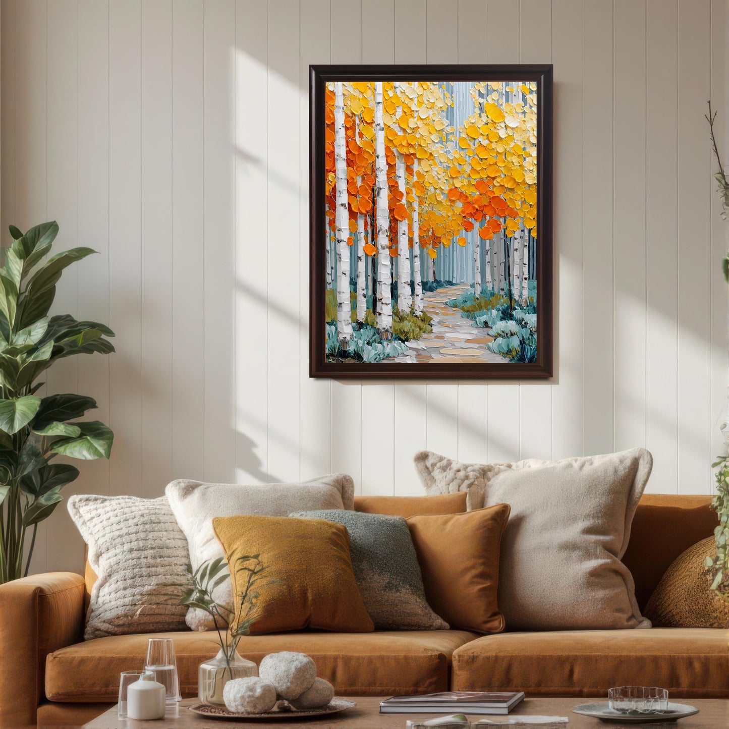 A framed print of an aspen forest with bright orange and yellow leaves hanging above a mustard-colored sofa in a bright living room. The frame is a dark brown (Coffee) color. Sunlight casts strong shadows across the white paneled wall.