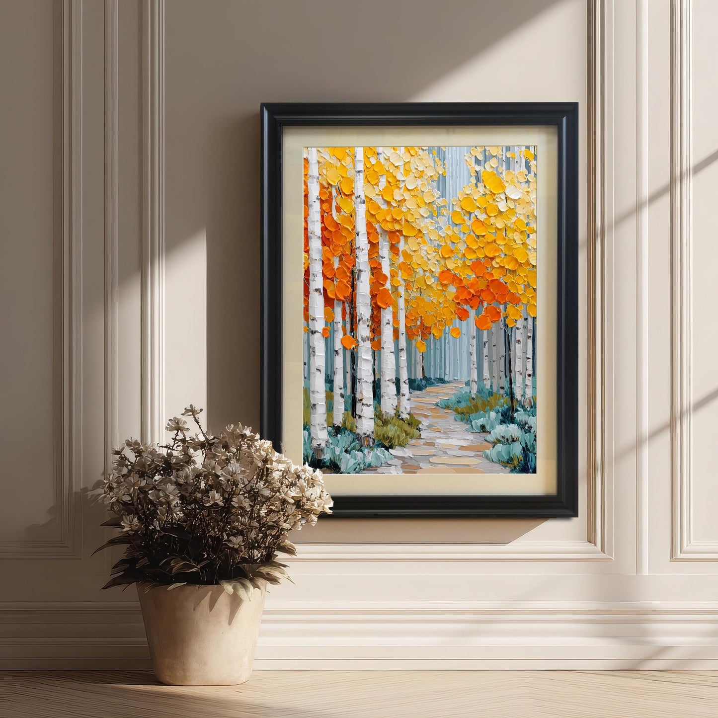 A framed print of an aspen forest, featuring thick, textured strokes of bright yellow and orange leaves and white birch trunks, leaning on a wooden floor against a white paneled wall. The frame is black with a beige mount. A potted cluster of dried white flowers sits on the floor nearby.