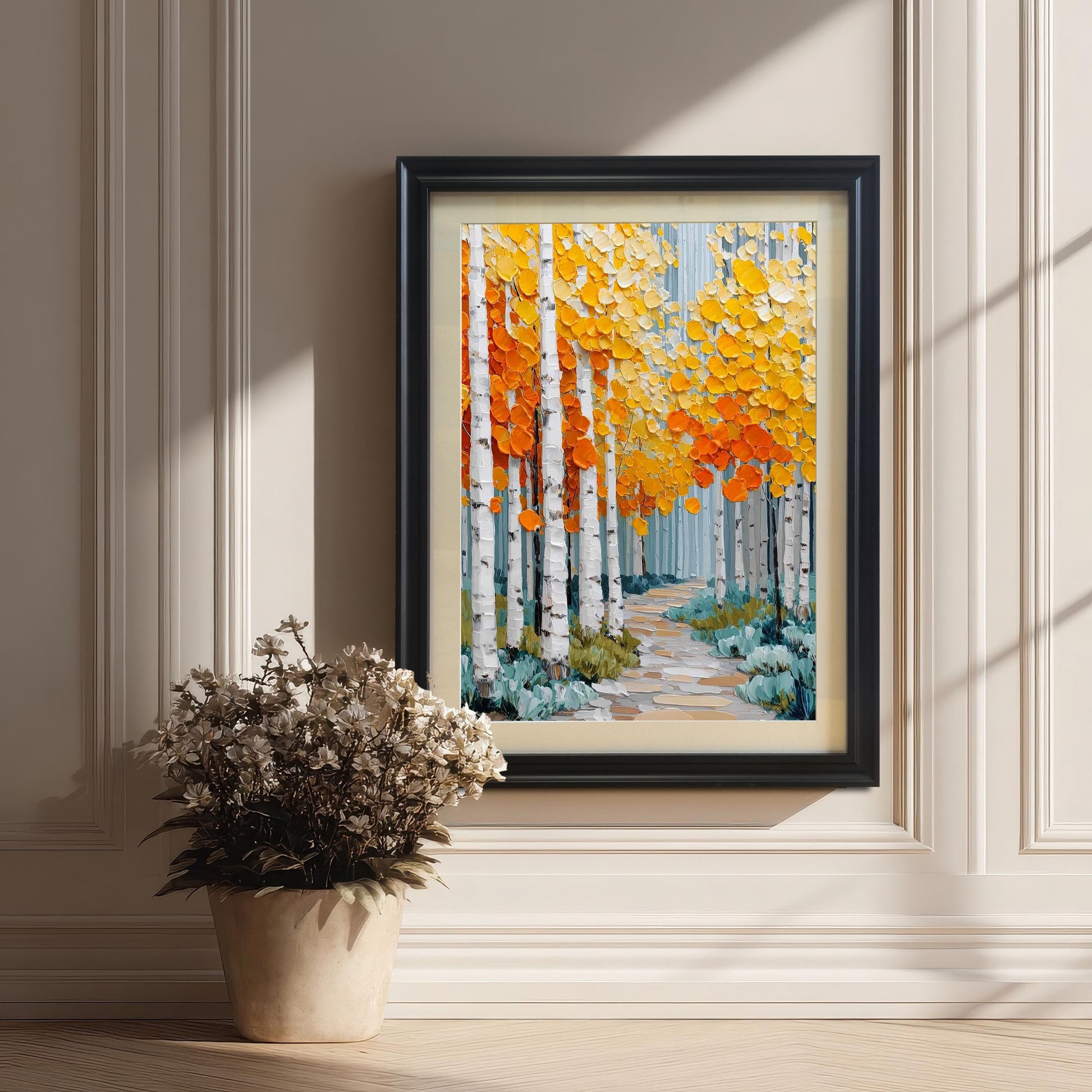A framed print of an aspen forest, featuring thick, textured strokes of bright yellow and orange leaves and white birch trunks, leaning on a wooden floor against a white paneled wall. The frame is black with a beige mount. A potted cluster of dried white flowers sits on the floor nearby.