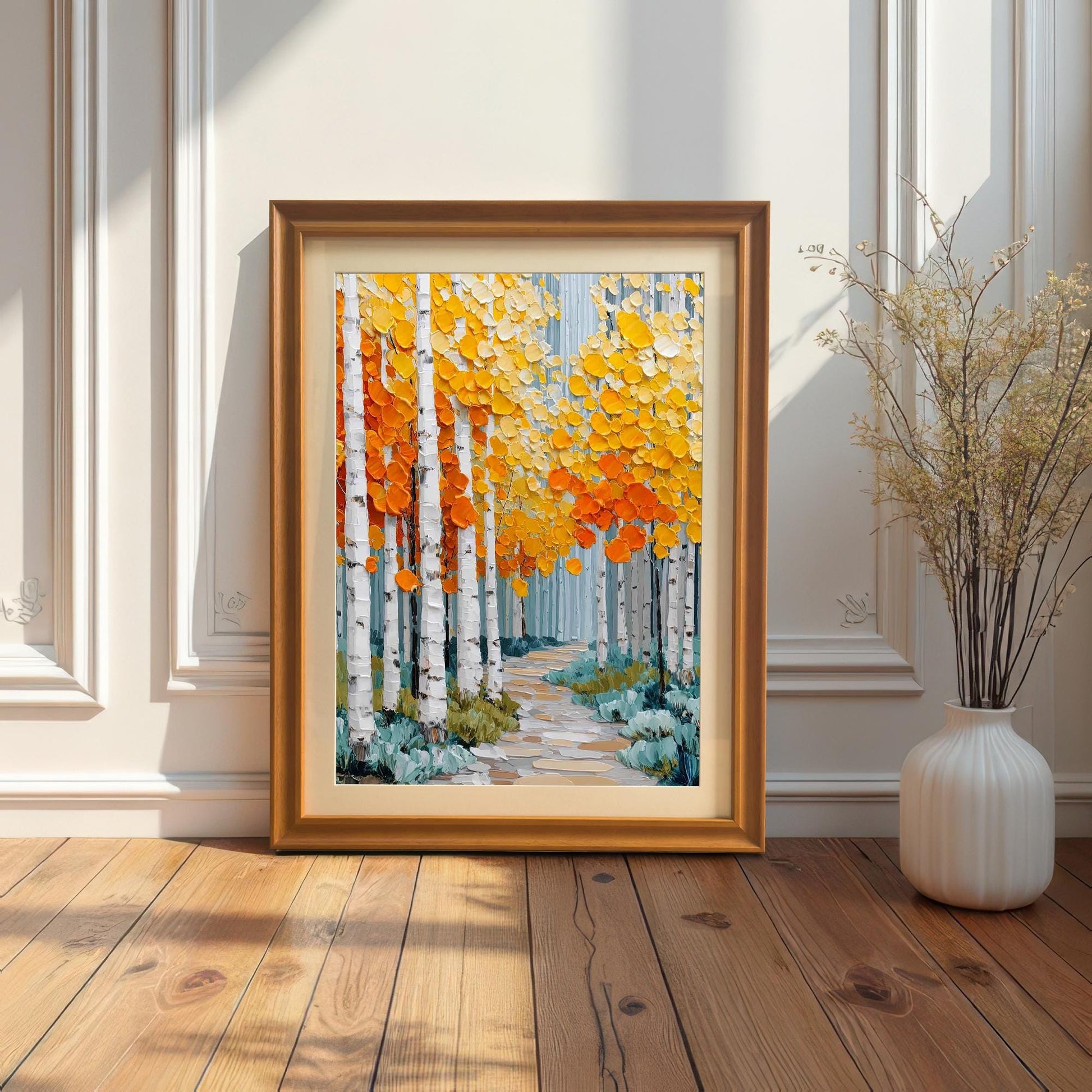 A framed print of an autumnal aspen forest leaning on a wooden floor against a white paneled wall. The frame is a gold/bronze color. A thin, dried floral arrangement in a tall white vase is to the right.