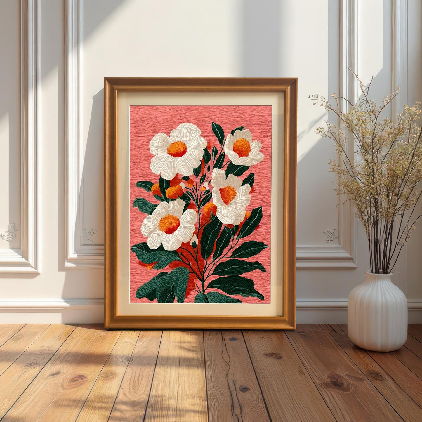 A framed floral print with a gold/bronze frame leaning on a wooden floor against a white paneled wall. A thin, dried floral arrangement in a white vase is to the right.