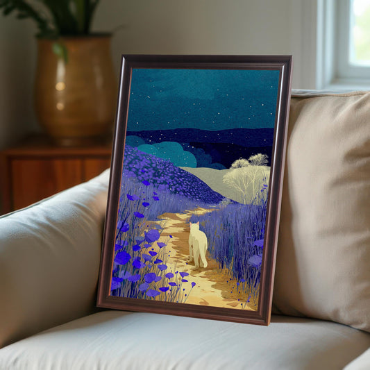 Framed print of a white cat walking on a path through fields of purple flowers under a starry, dark blue night sky. The print is leaning against a light-colored couch. The frame is dark brown or coffee-colored.