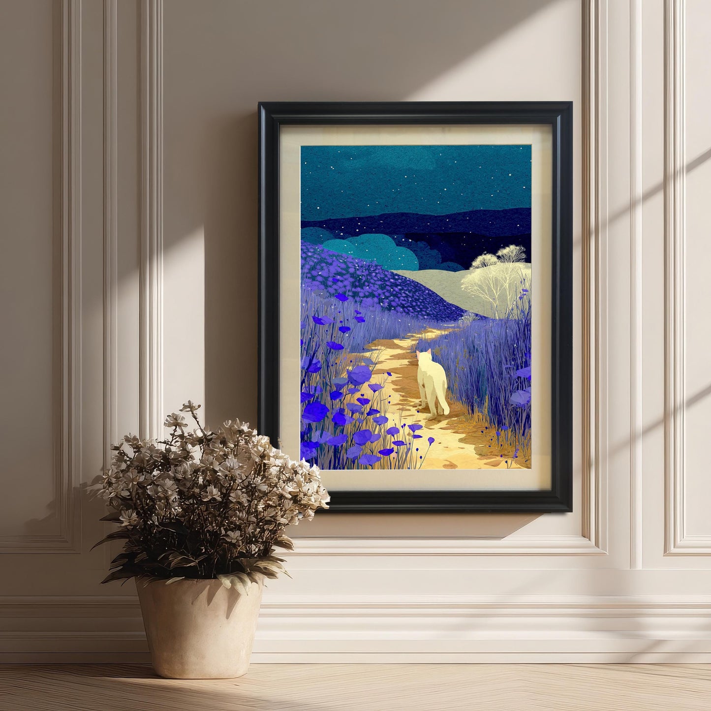 A framed print of the night landscape art is hanging on a classic white wall with wainscoting. The frame is black and includes a light-colored mount. A potted plant with dried flowers sits on the floor to the left.