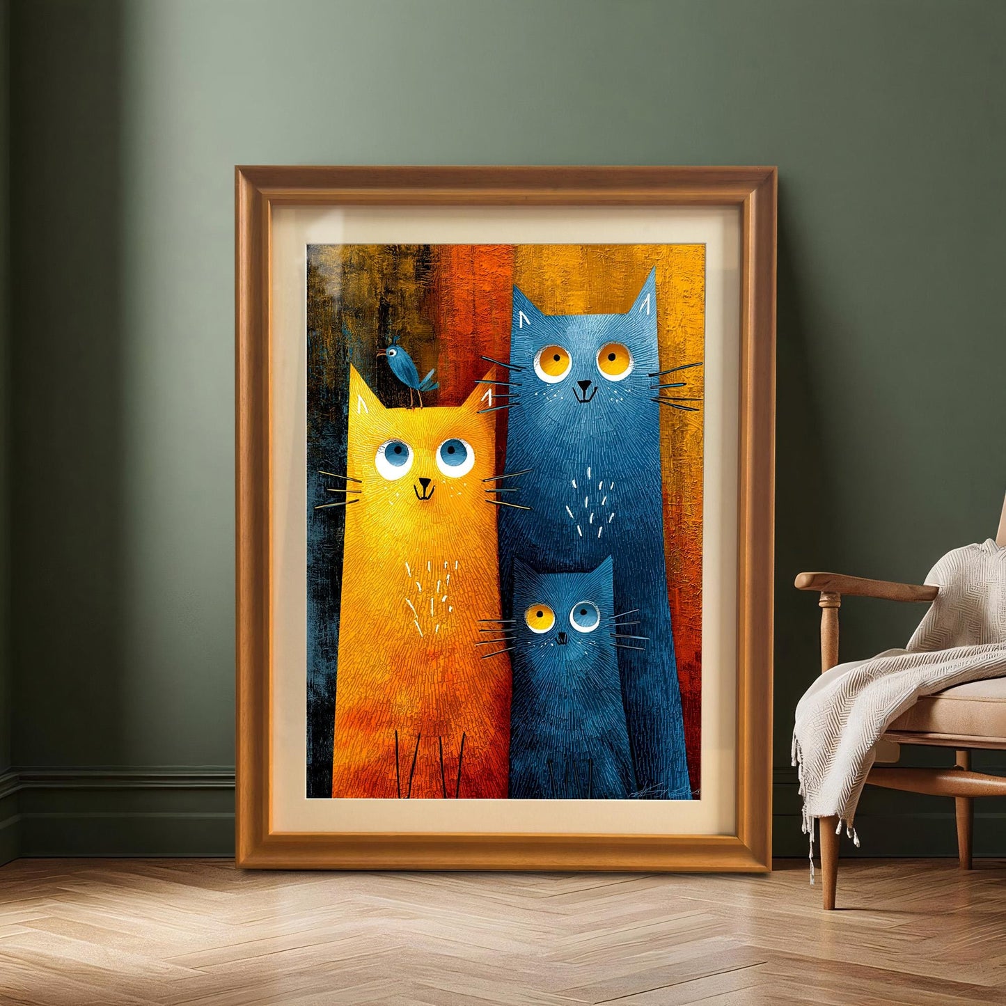 A large framed print of the cat family art, with an orange-gold frame and a mount, is leaning on the floor against a dark green accent wall. A wooden armchair and a throw blanket are visible on the right.