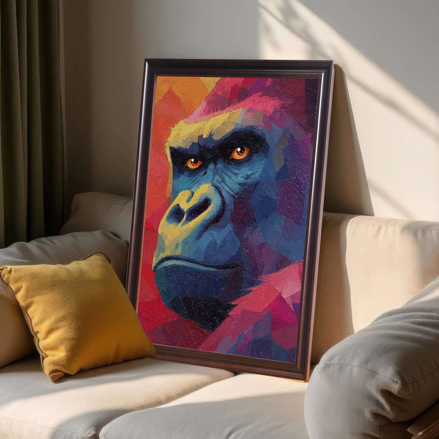 Close-up studio shot of a framed, vibrant, colorful oil-painting-style print of a gorilla's face, leaning against a neutral-colored couch in a sunlit room. The frame appears to be dark brown or coffee-colored.