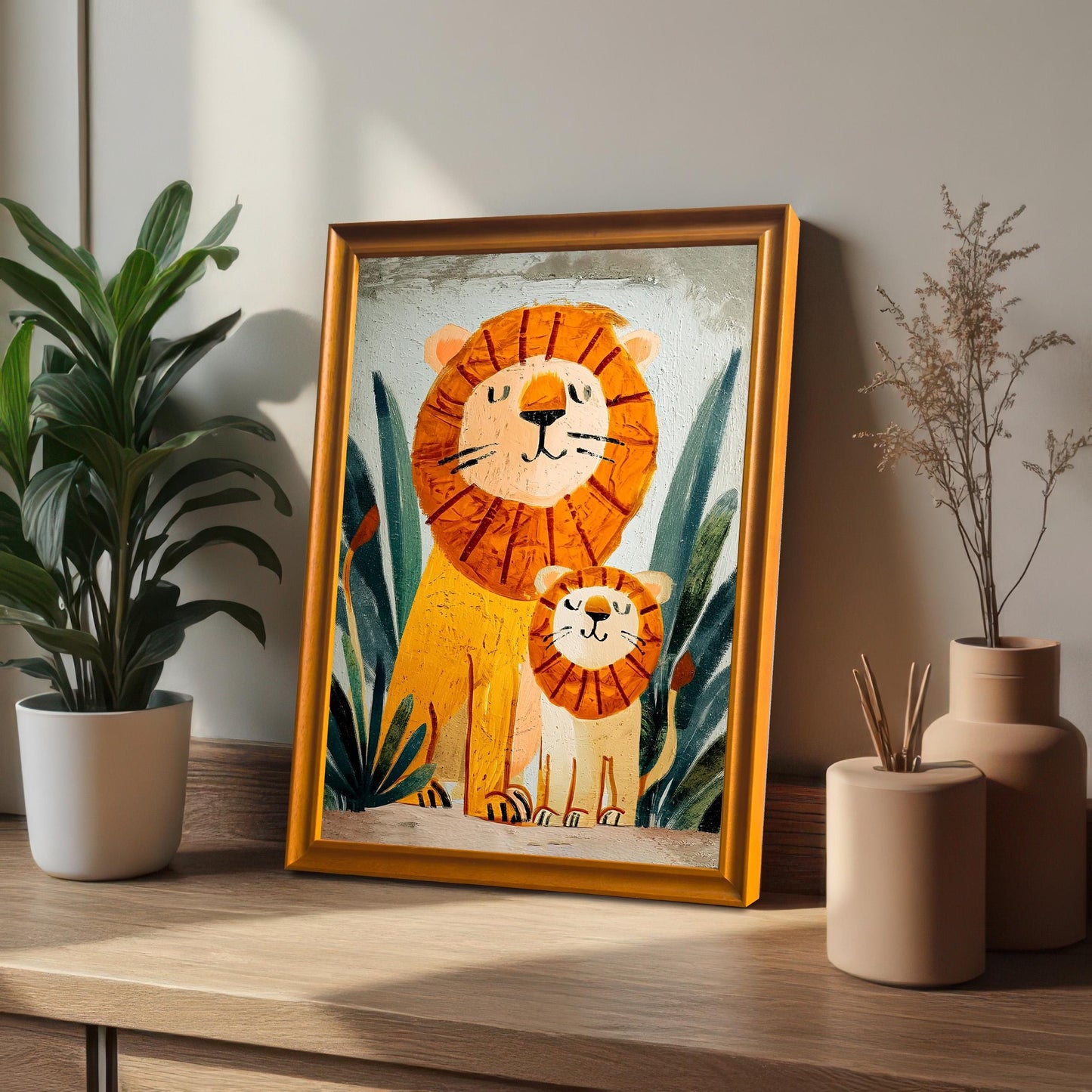 Close-up of a framed print featuring the lion and cub in a gold-colored frame, leaning against a wall on a wooden surface next to a potted houseplant and neutral-toned vases.