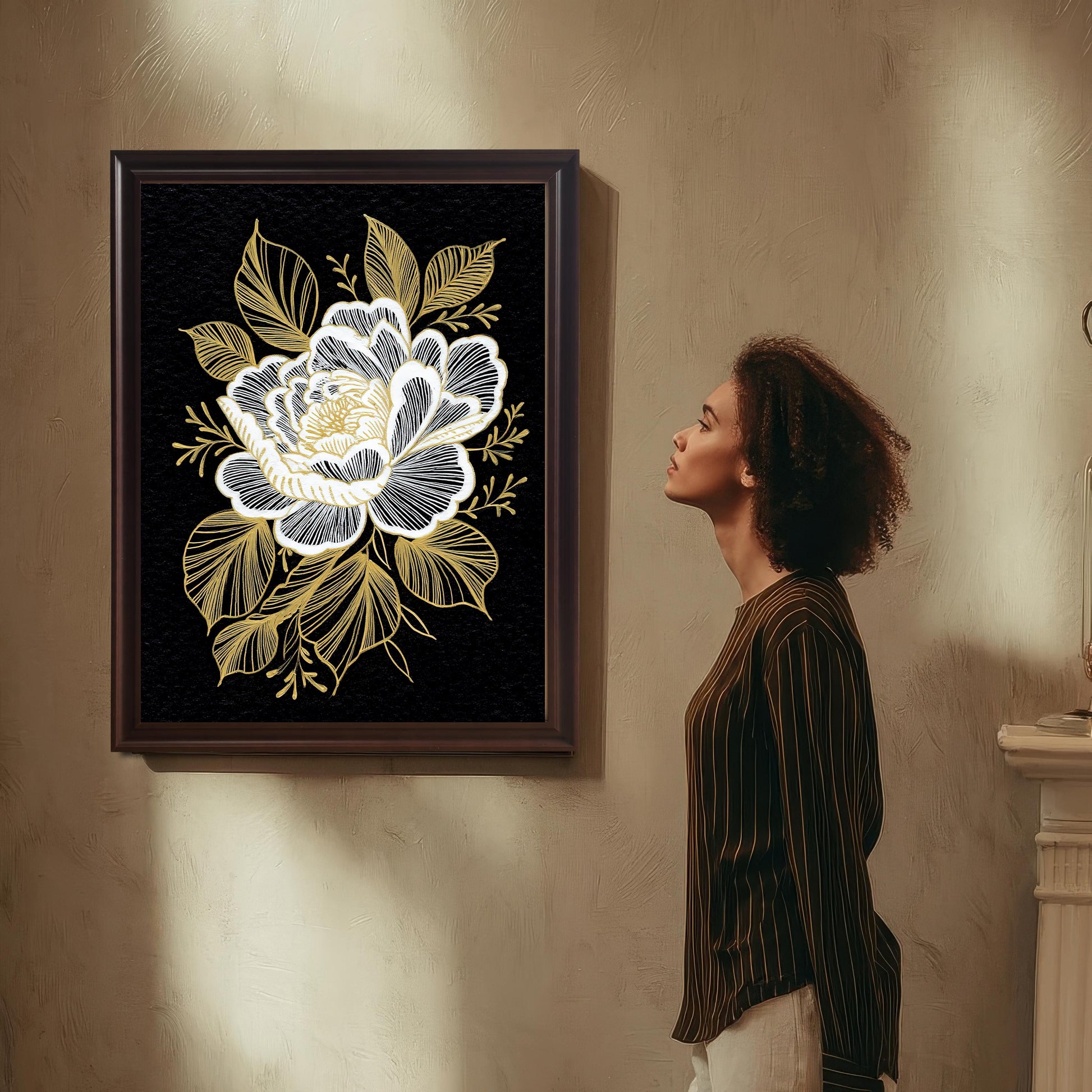 A woman with curly hair, wearing a striped shirt and light-colored pants, stands in profile admiring the black and gold floral print, which is framed in a dark Coffee Frame and hung on a textured beige wall.