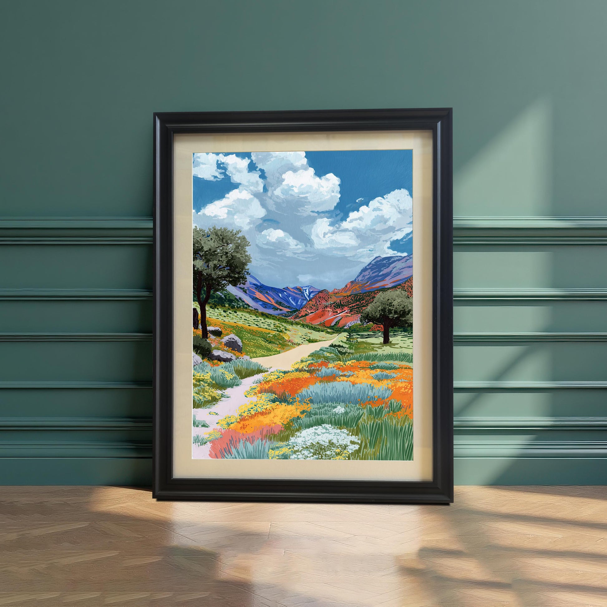 A colorful painting of a path winding through a field of orange and yellow wildflowers, framed in a Black frame with a mount, leaning on a hardwood floor against a decorative dark green paneled wall.