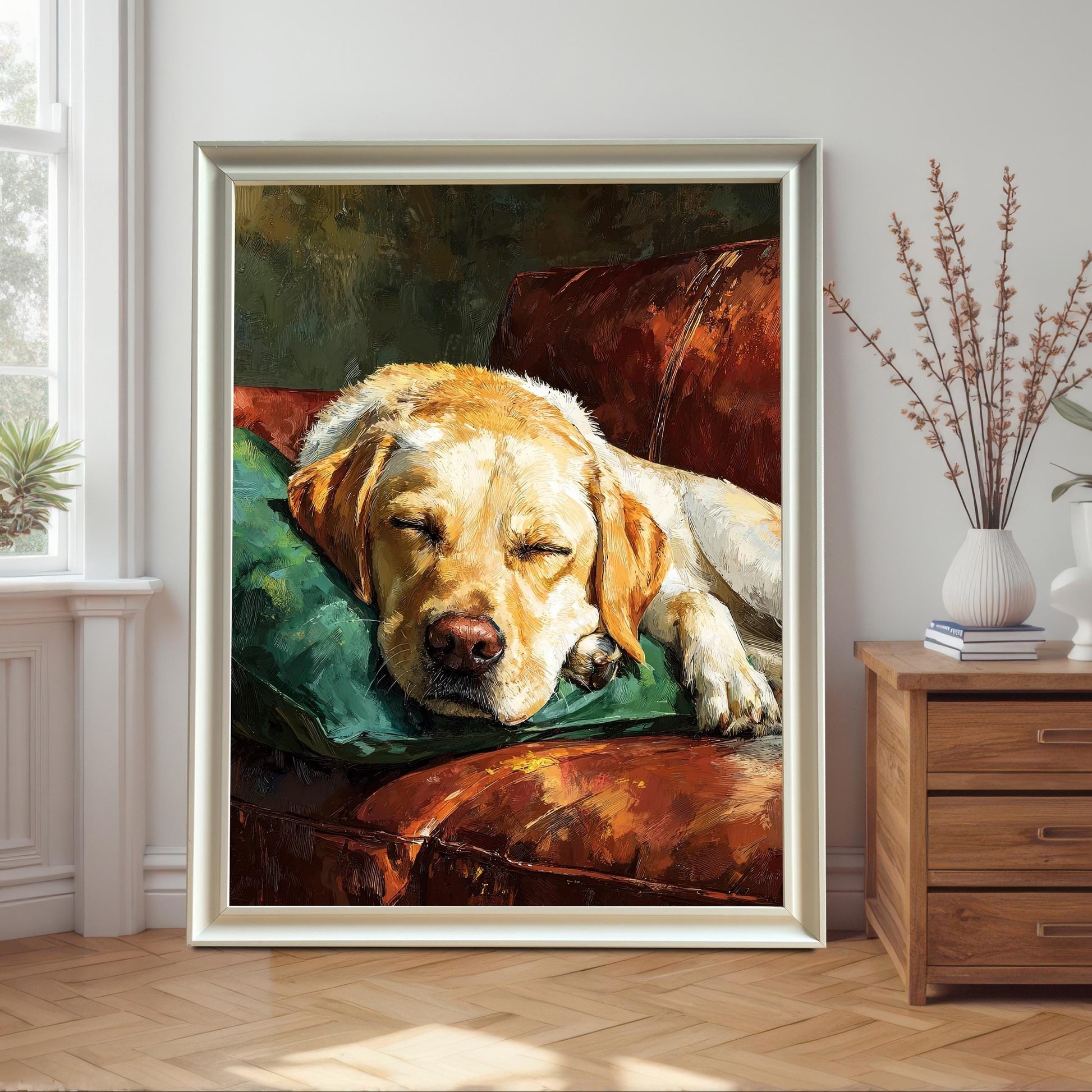 A white-framed painting of a yellow Labrador dog sleeping on a green pillow on a brown leather couch, leaning on a wall next to a wooden nightstand.