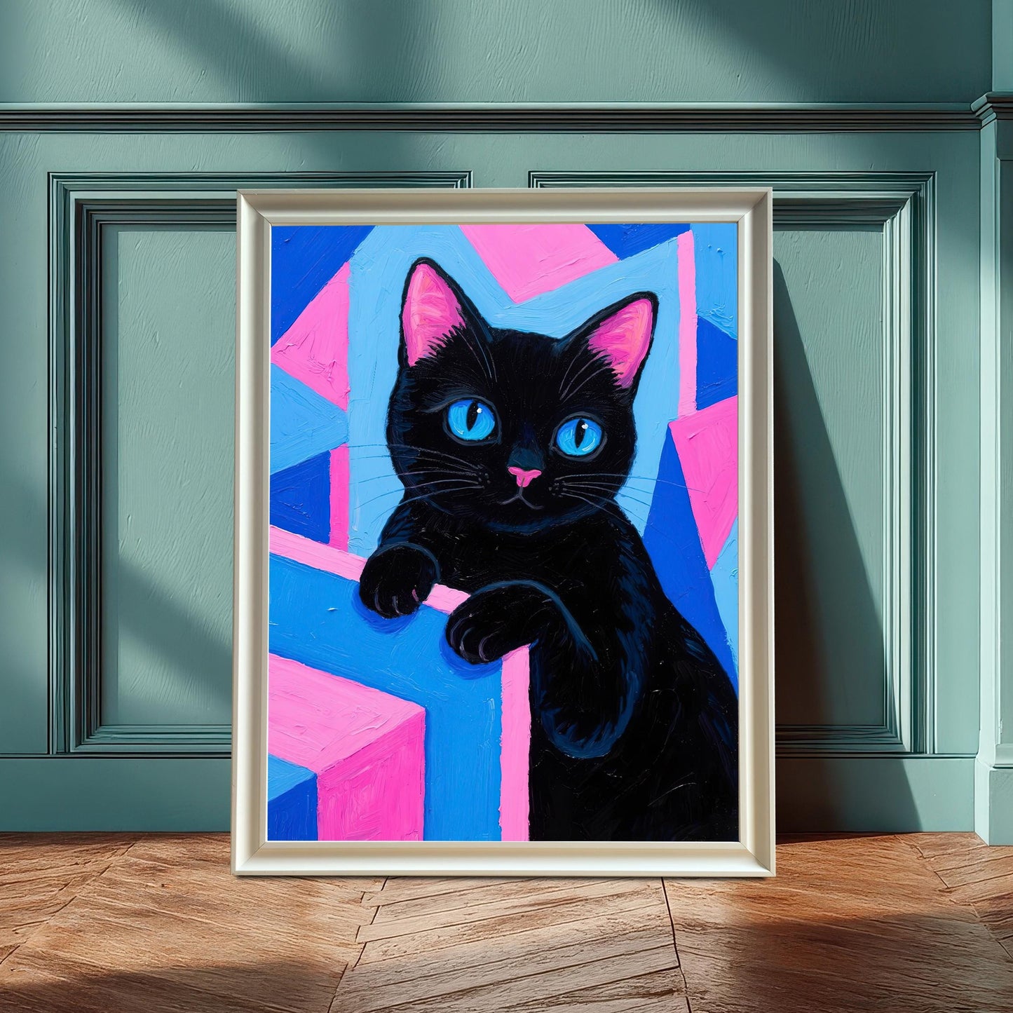 A framed art print of a black cat with blue eyes on a pink and blue geometric background, in a white frame leaning against a teal wainscoting wall.