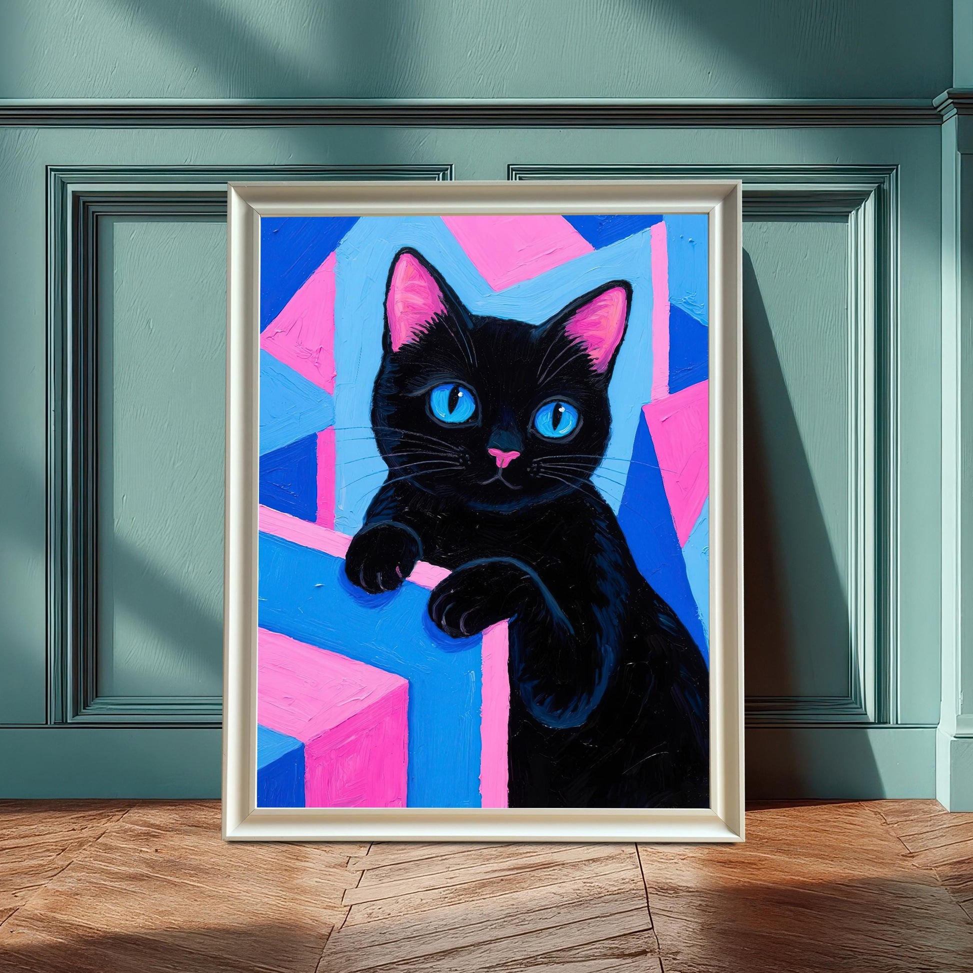 A framed art print of a black cat with blue eyes on a pink and blue geometric background, in a white frame leaning against a teal wainscoting wall.