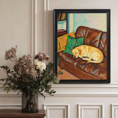 A large, black-framed art print of an oil painting of a yellow Labrador sleeping on a brown leather couch, hanging on a paneled wall near a vase of flowers.
