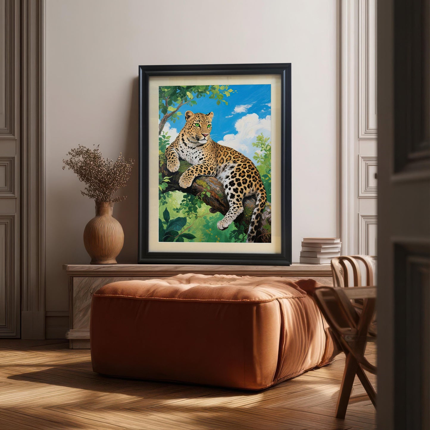 A large framed black and leopard print is propped on a low console behind a leather ottoman in a sunlit room.