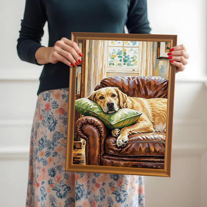A woman holds an orange-brown framed painting of a Labrador Retriever relaxing on a leather armchair with a green pillow.