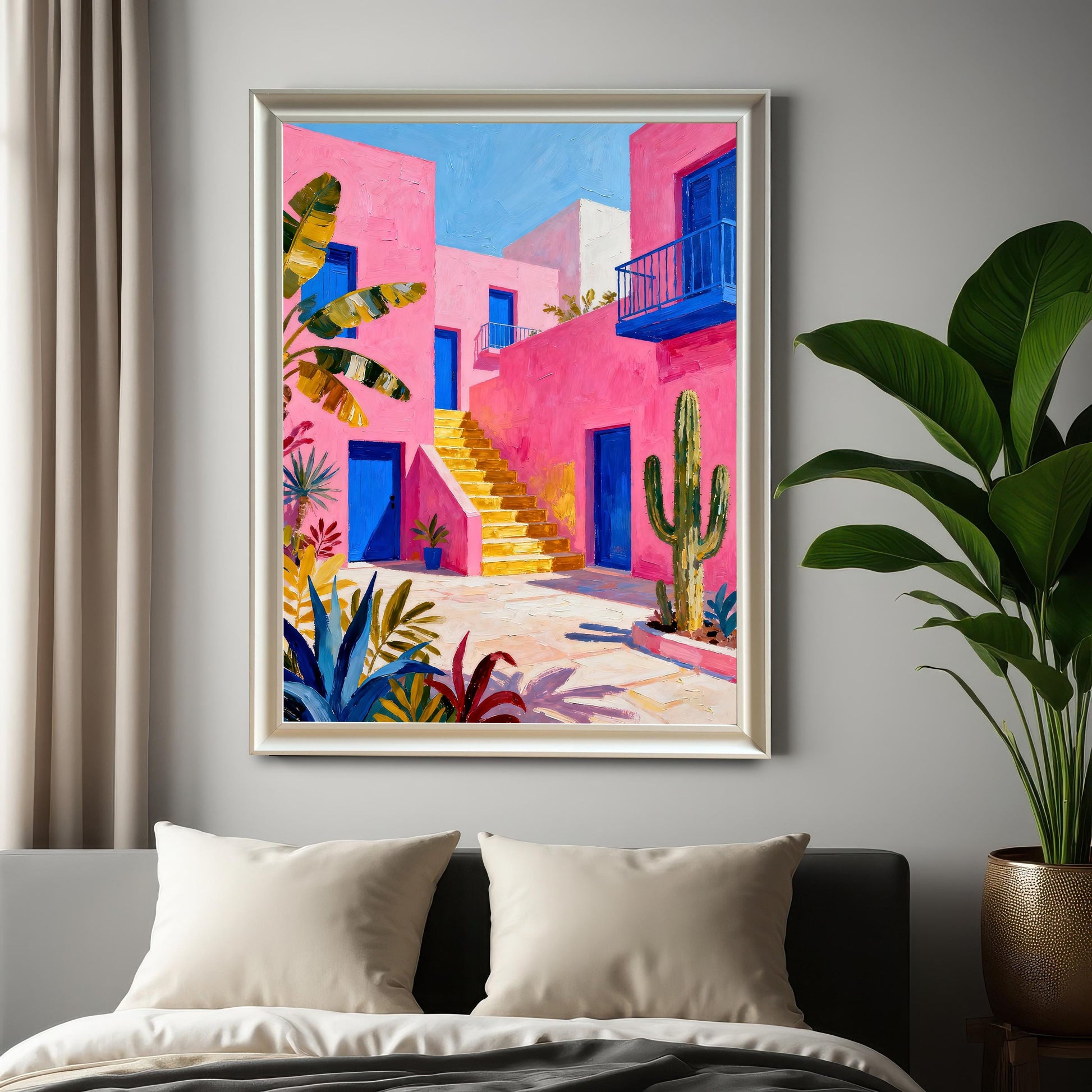 A framed print of a vibrant pink building with blue doors and yellow stairs, hanging on a gray wall above a bed, displayed in a White Frame / No Mount next to a large potted plant.