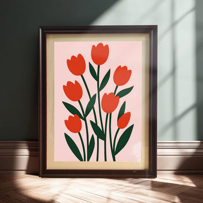 A dark-framed print of red tulips on a pink background is leaning on a wooden floor against a dark green wall, with natural sunlight casting strong shadows.