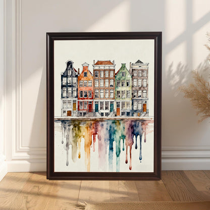 Watercolor art print featuring a row of colorful, historic European canal houses (like Amsterdam or Ghent) with a mirrored reflection dissolving into vibrant, dripping rainbow colors. The print is in a dark frame leaning on a wooden floor against a white paneled wall.