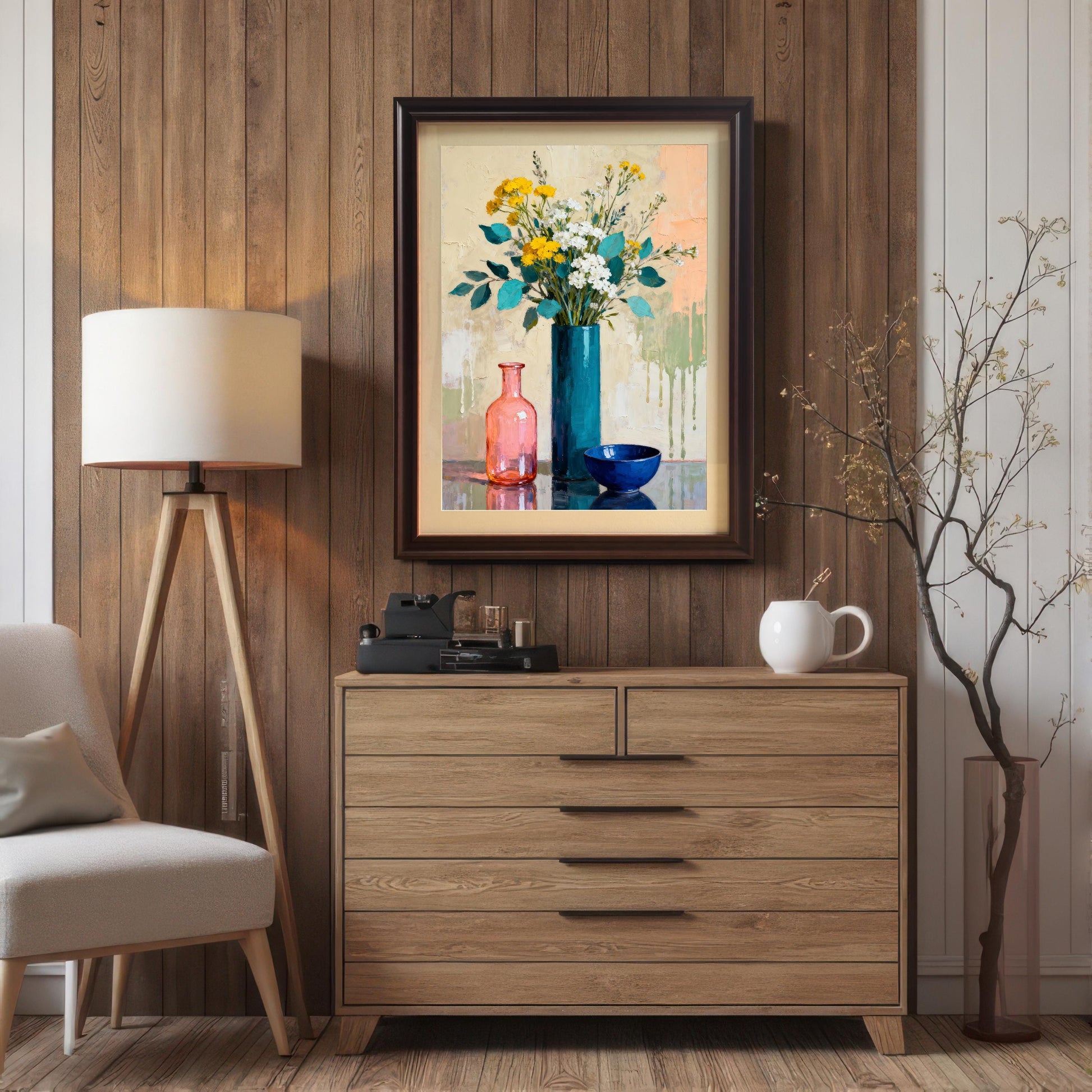 Framed art print in a Coffee wood frame hanging above a light wooden dresser, next to a tripod floor lamp, in a room with vertical wood paneling.
