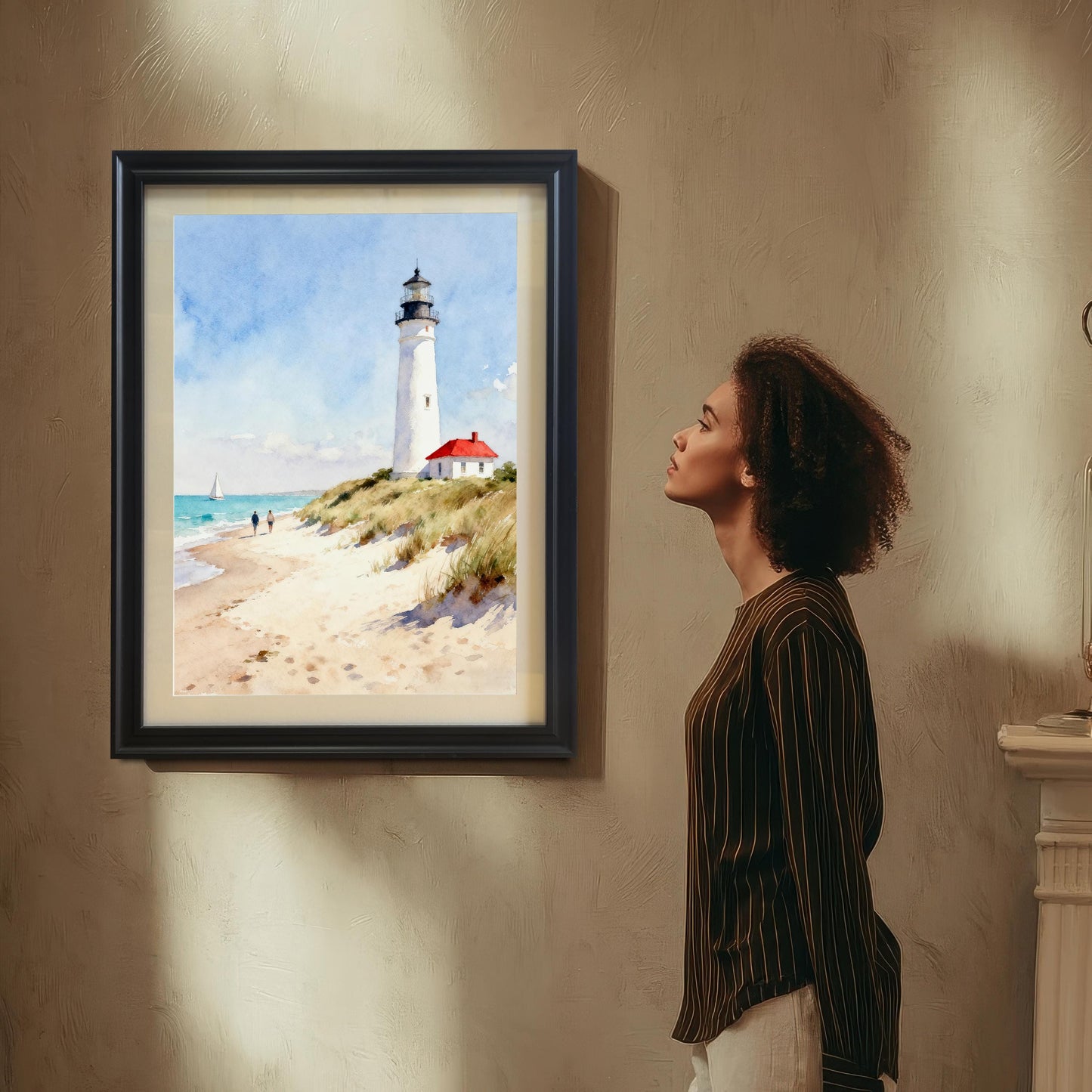 Lifestyle photo showing a woman looking at the framed art print of a lighthouse on a beach, which is hung on a beige wall in a black frame.