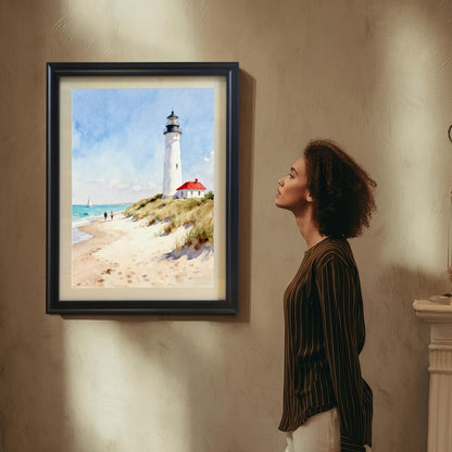 Lifestyle photo showing a woman looking at the framed art print of a lighthouse on a beach, which is hung on a beige wall in a black frame.