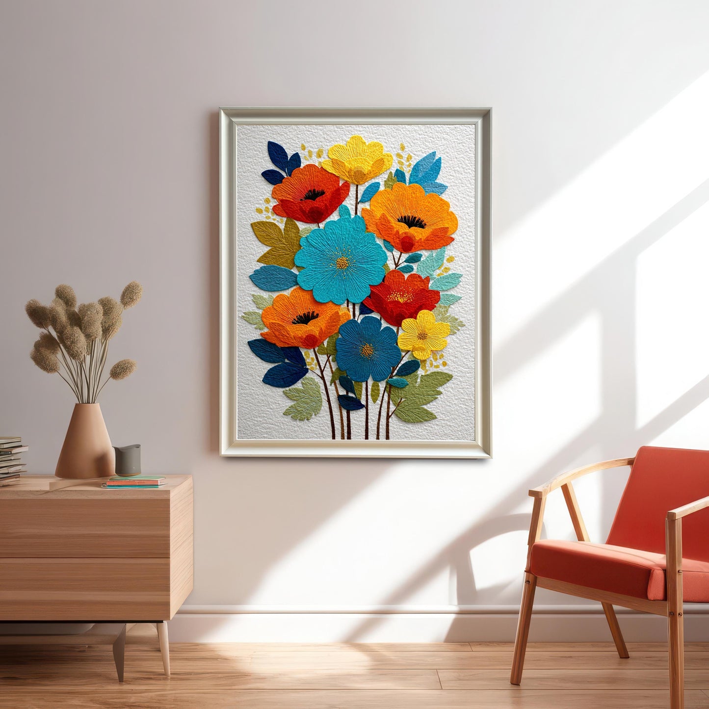 A framed art print of colorful embroidered-style flowers (red, orange, blue, yellow) hanging on a white wall in a modern living space with a wooden side table and an orange accent chair.