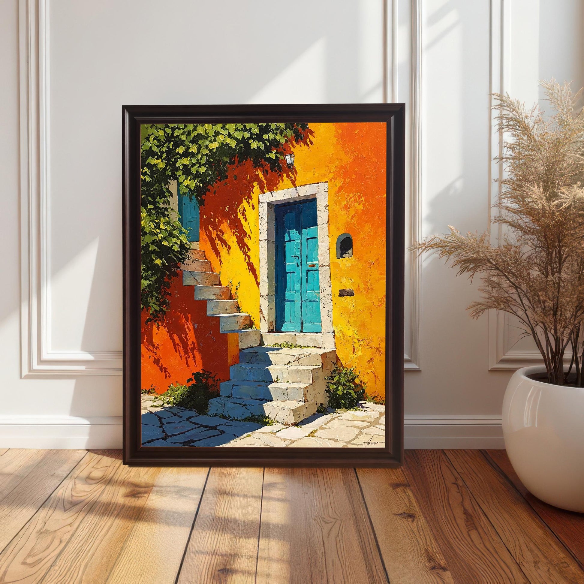 tylized photo of the framed art print (Coffee frame with a mount) resting on a hardwood floor against a white wainscoted wall. The art features a vibrant orange and yellow wall, turquoise blue door, and stone steps, next to a dried grass arrangement in a large white pot.