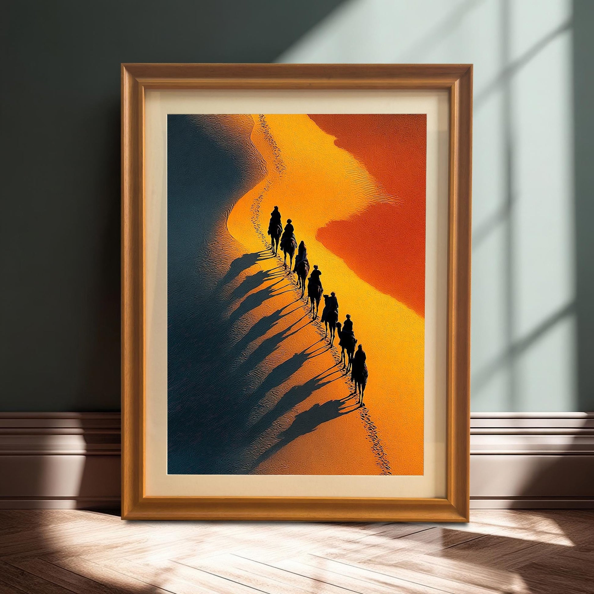 Stylized photo of the framed desert art print (Orange Frame & Mount) resting on a wooden floor against a dark wall, illuminated by a strong sunlight shadow. The art shows a line of camels with long shadows on a sandy dune.
