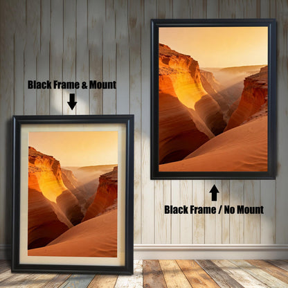 Two framed prints of a slot canyon landscape at sunset showing layers of orange and red rock formations with mist. The left shows a Black Frame & Mount (matting), and the right shows a Black Frame / No Mount.