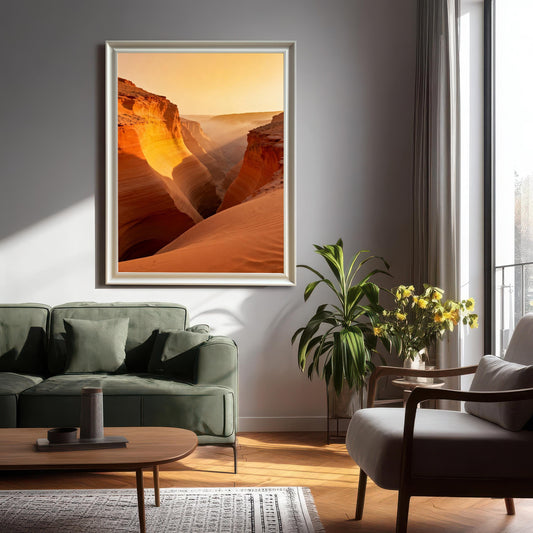 Large framed print of the vibrant canyon with mist and sunlight hanging on a light grey wall in a living room setting with a green sofa and plant. The frame is White-colored wood.