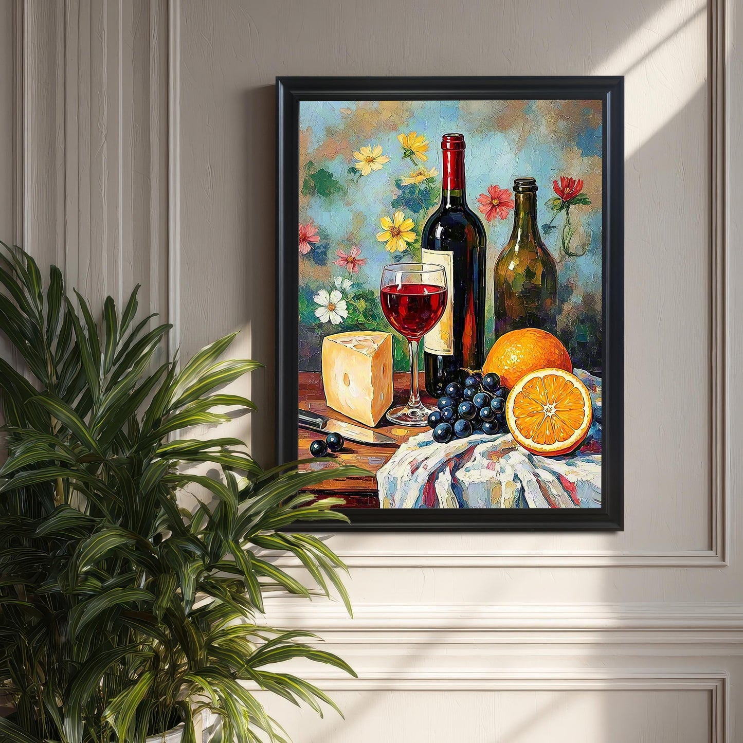 The vibrant oil painting of a wine still life with cheese, grapes, and oranges, framed in a black wood frame with no mount. The framed print is hanging on a textured gray wall, partially obscured by a large green houseplant in the foreground.