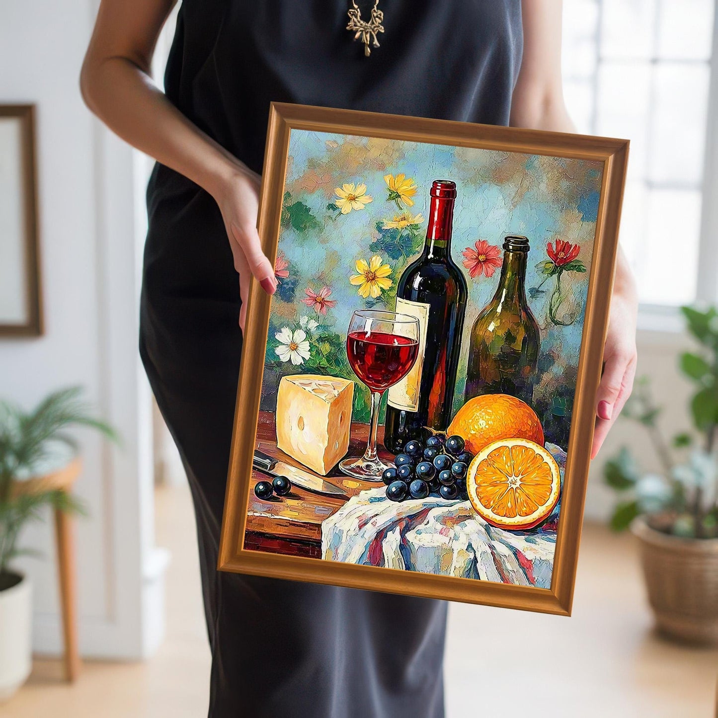 Close-up of a person holding the still life wine and fruit art print in a gold/orange wood frame. The person is wearing a black dress.