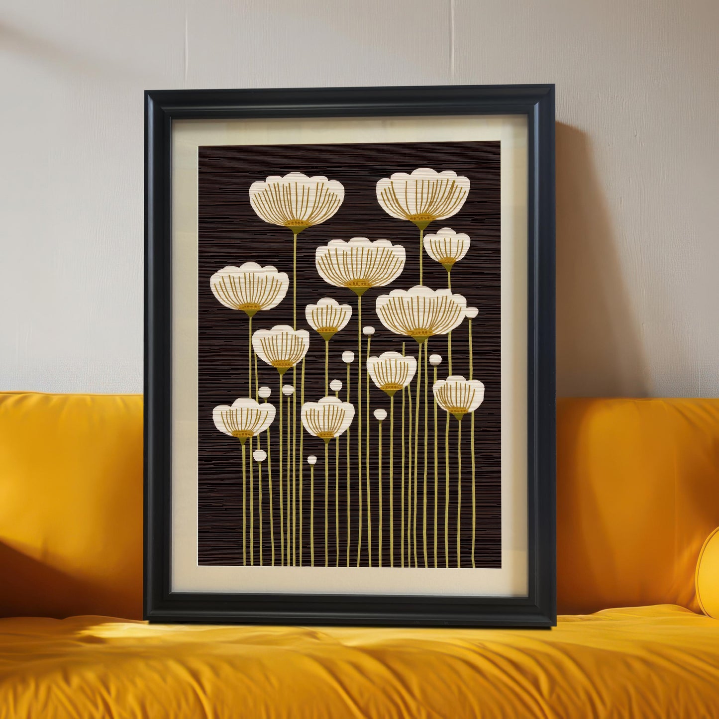 Black framed art print of abstract white and gold flowers, leaning on the floor against a bright yellow couch.