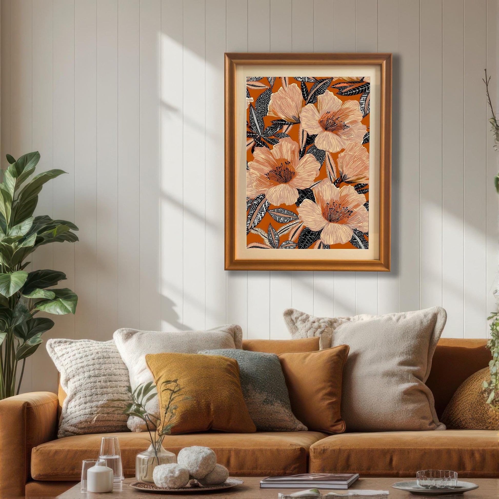 Lifestyle photo of the floral art print in an Orange wood frame hanging above a rust-colored sofa with neutral and yellow cushions in a bright living room. The print has peach-colored flowers on a bold orange background.