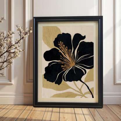 The black and gold abstract floral art print in a Black Frame with a Mount (matting) rests on a wooden floor against a white paneled wall. A branch with small white blossoms is visible on the left, highlighting the contrast and natural aesthetic.