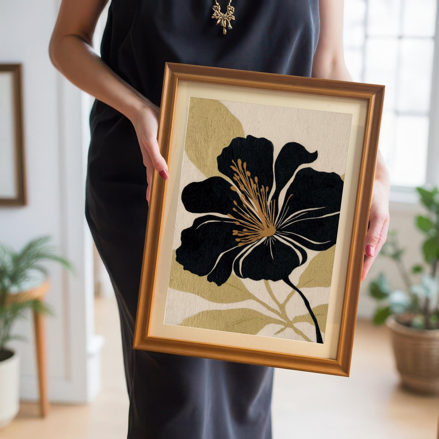 A person in a black dress holds the black and gold floral art print in a gold frame, showcasing the artwork's scale and frame color choice.