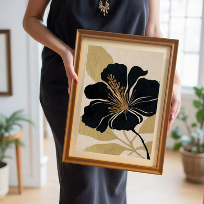 A person in a black dress holds the black and gold floral art print in a gold frame, showcasing the artwork's scale and frame color choice.